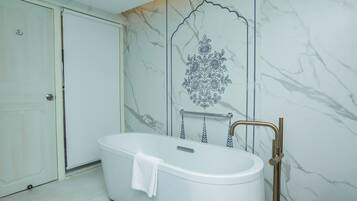 Une salle de bain avec une baignoire sur pieds, une serviette posée sur le bord, et une douche dotée d’un robinet doré.