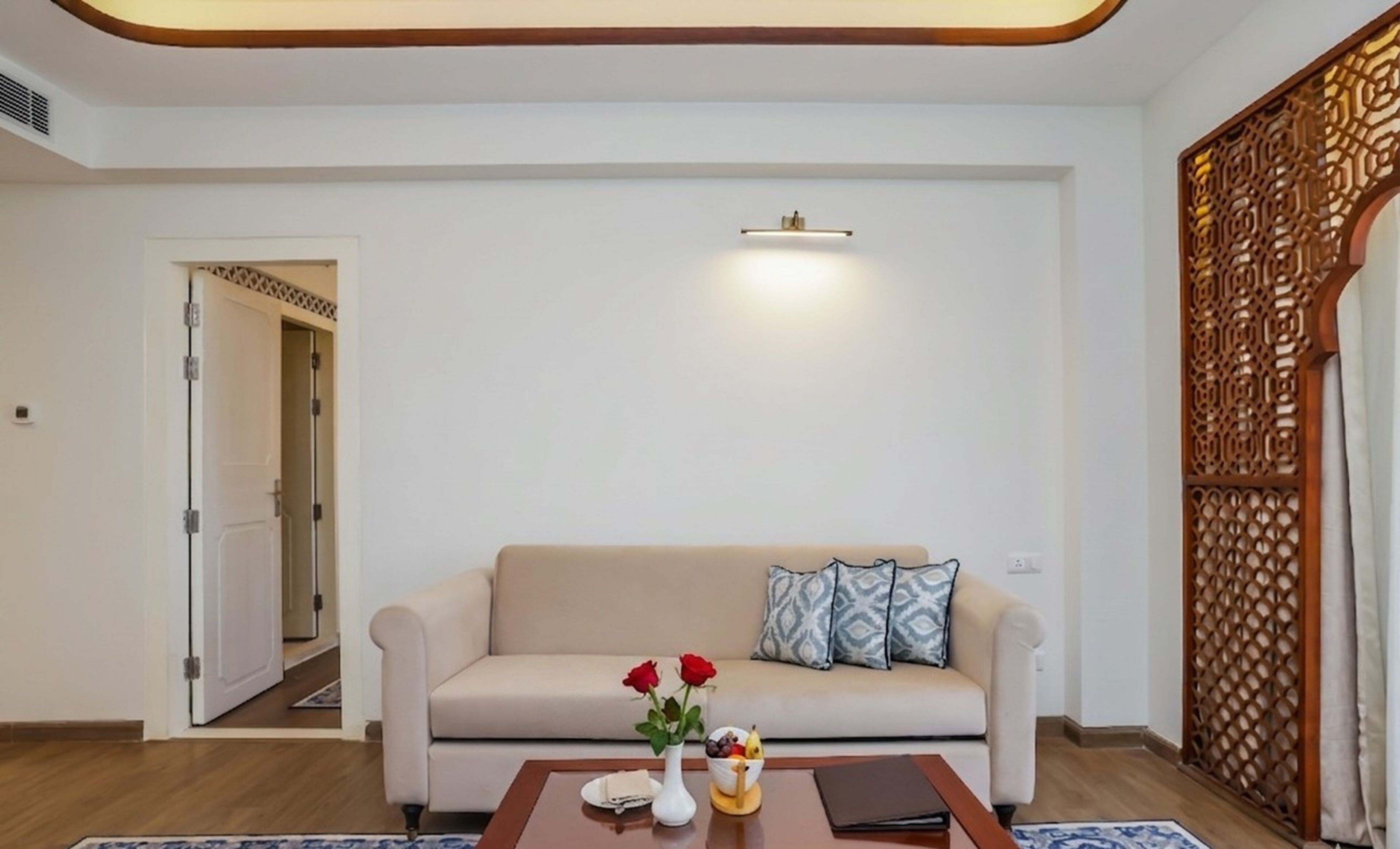 A living room with a beige sofa, a coffee table, a vase with flowers, and a decorative screen.