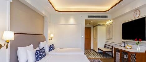 A hotel room with two beds, a TV, a desk with a vase, and a patterned rug.