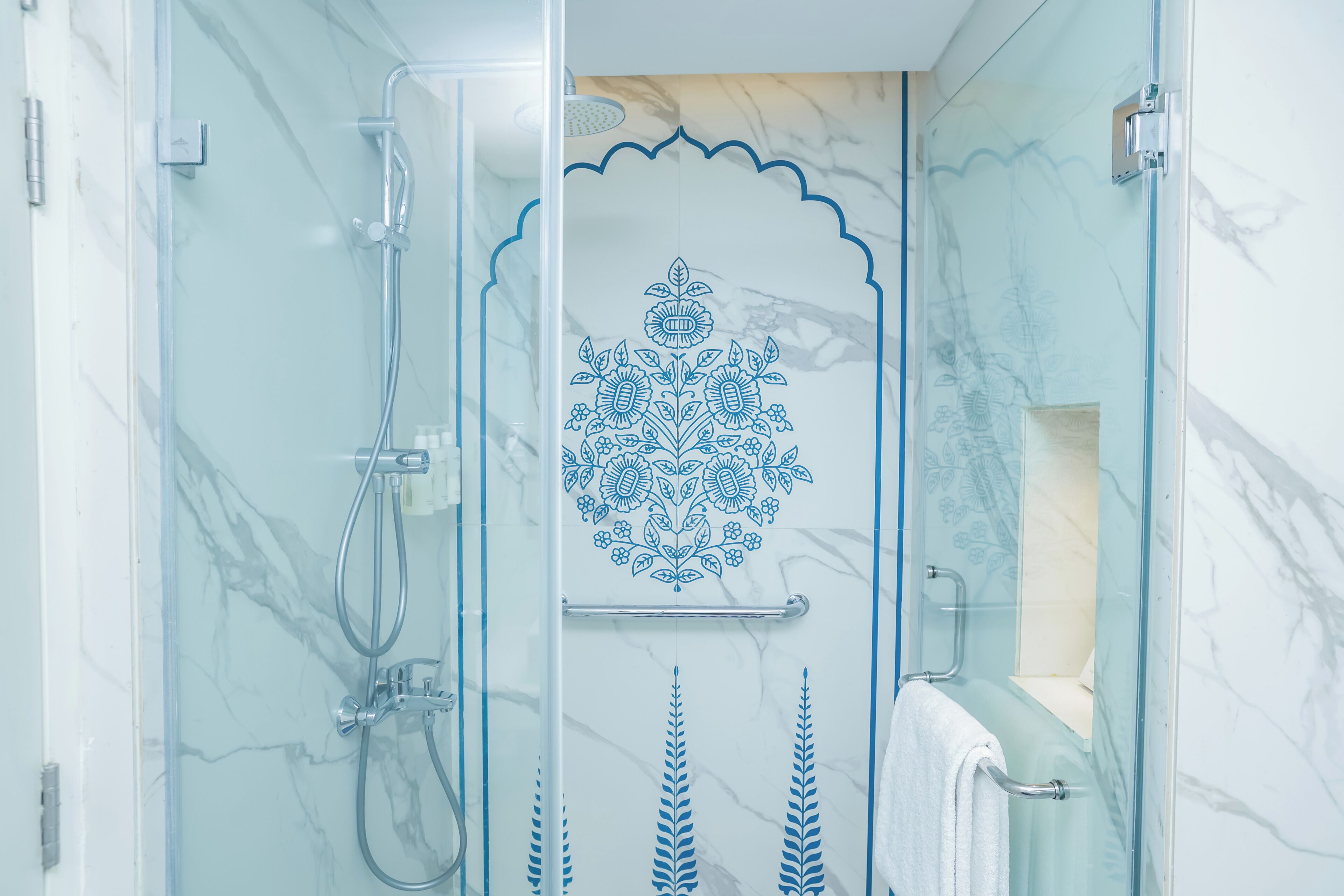 Une douche fermée par des parois de verre, agrémentée de carreaux décoratifs, avec un porte-serviettes et un mur en marbre.