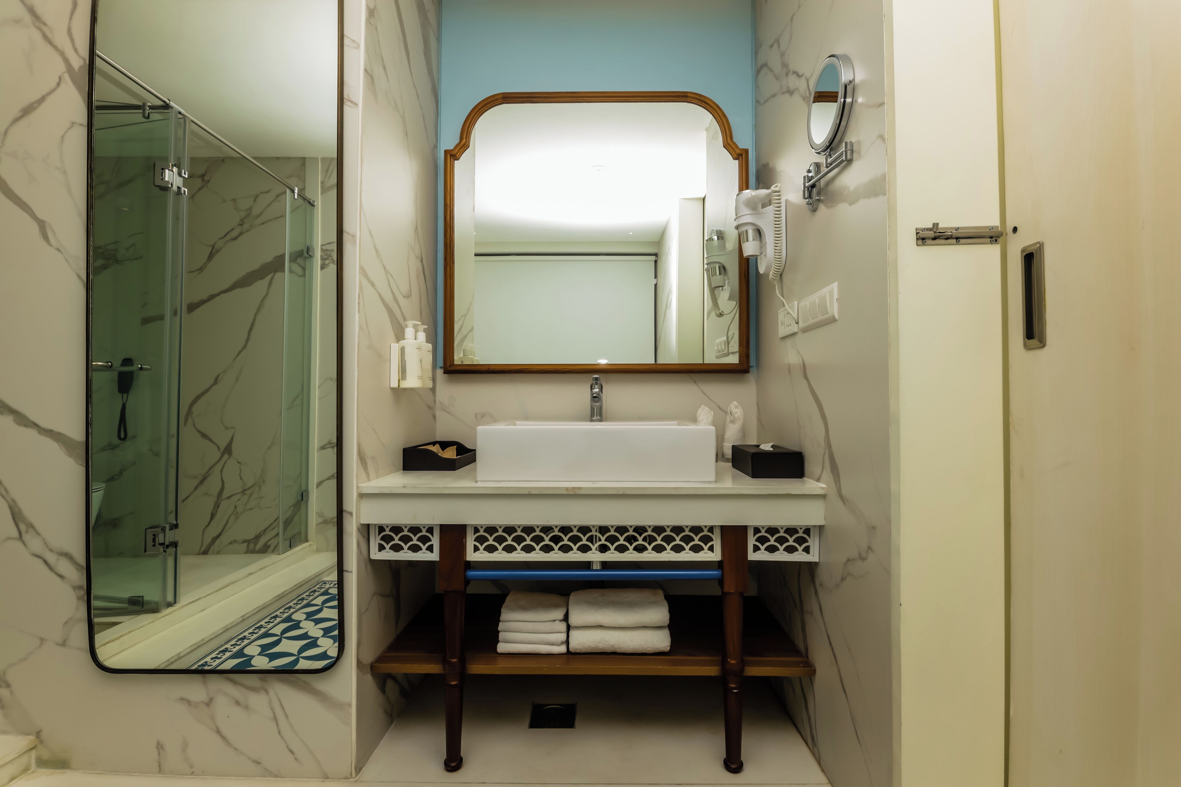 A bathroom with a glass shower enclosure, a white sink with a marble backsplash, and a mirror with a wooden frame.