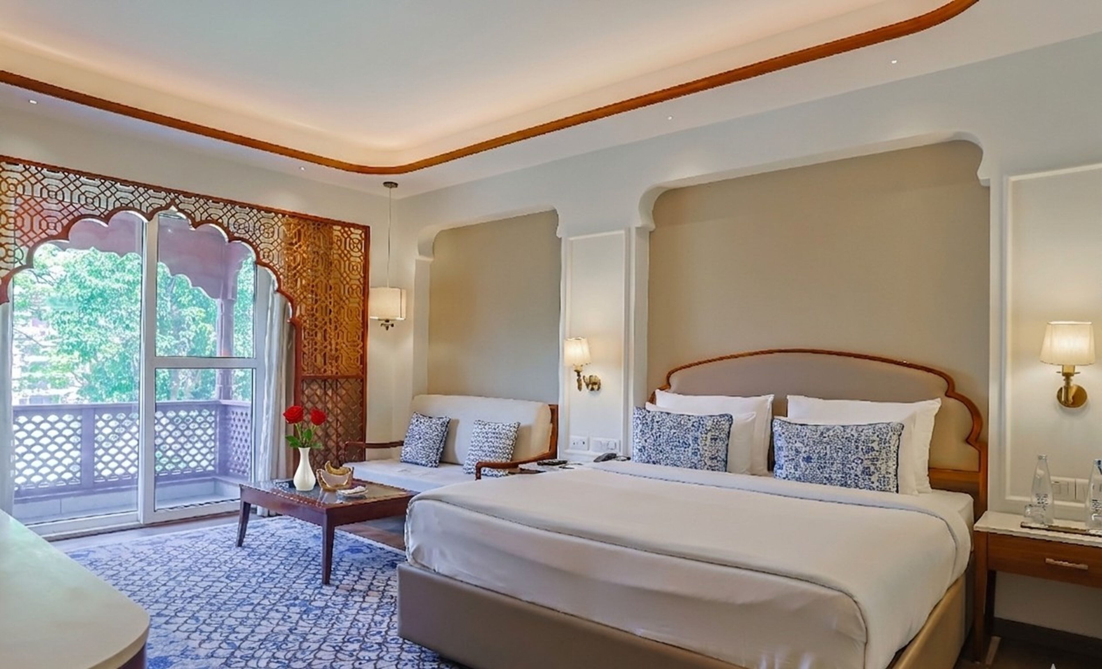 A hotel room with a large bed, a sitting area with a coffee table, and a view through a window with a decorative screen.