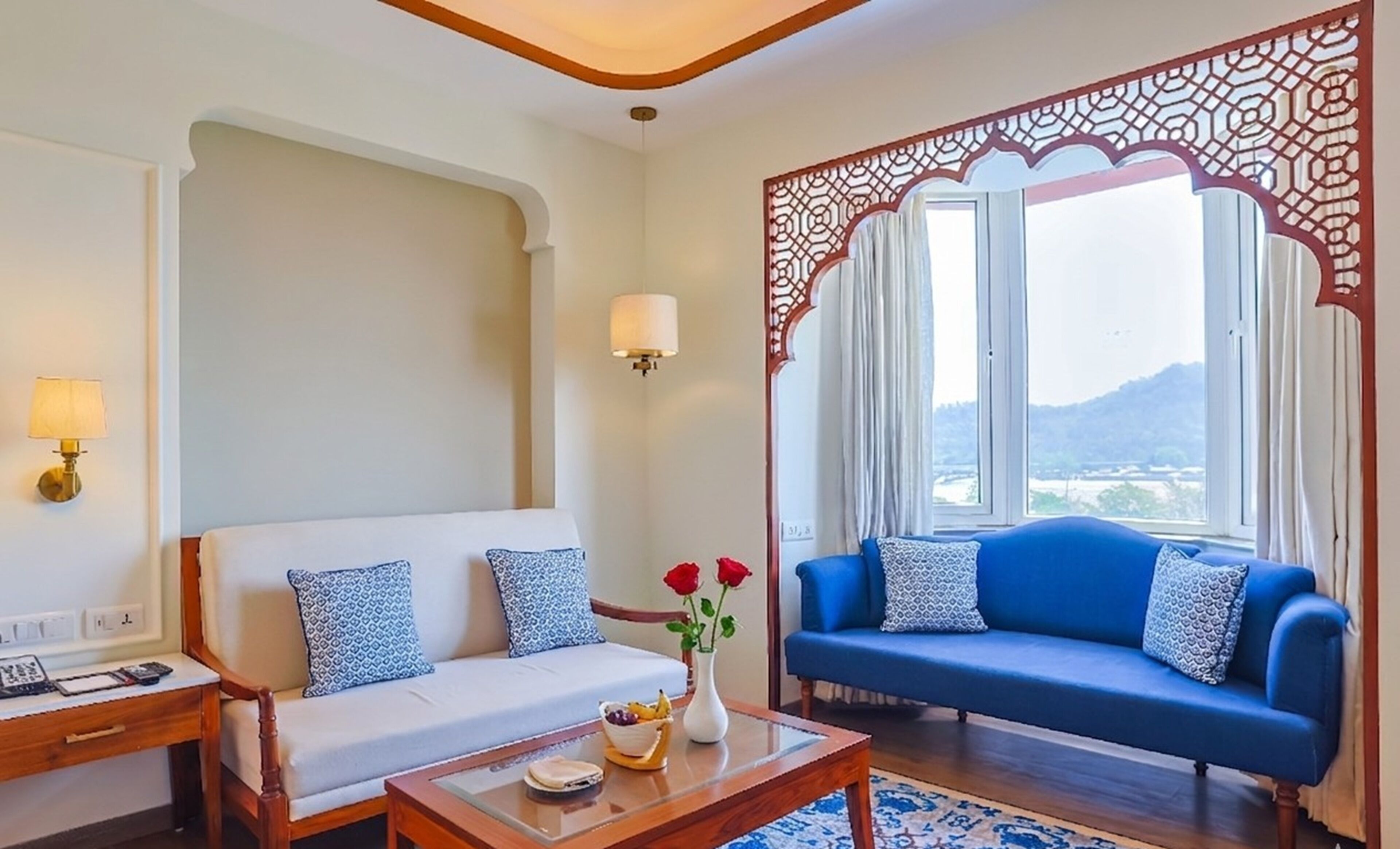 A room with a sofa, a coffee table with fruits, a lamp, and a window with a view.