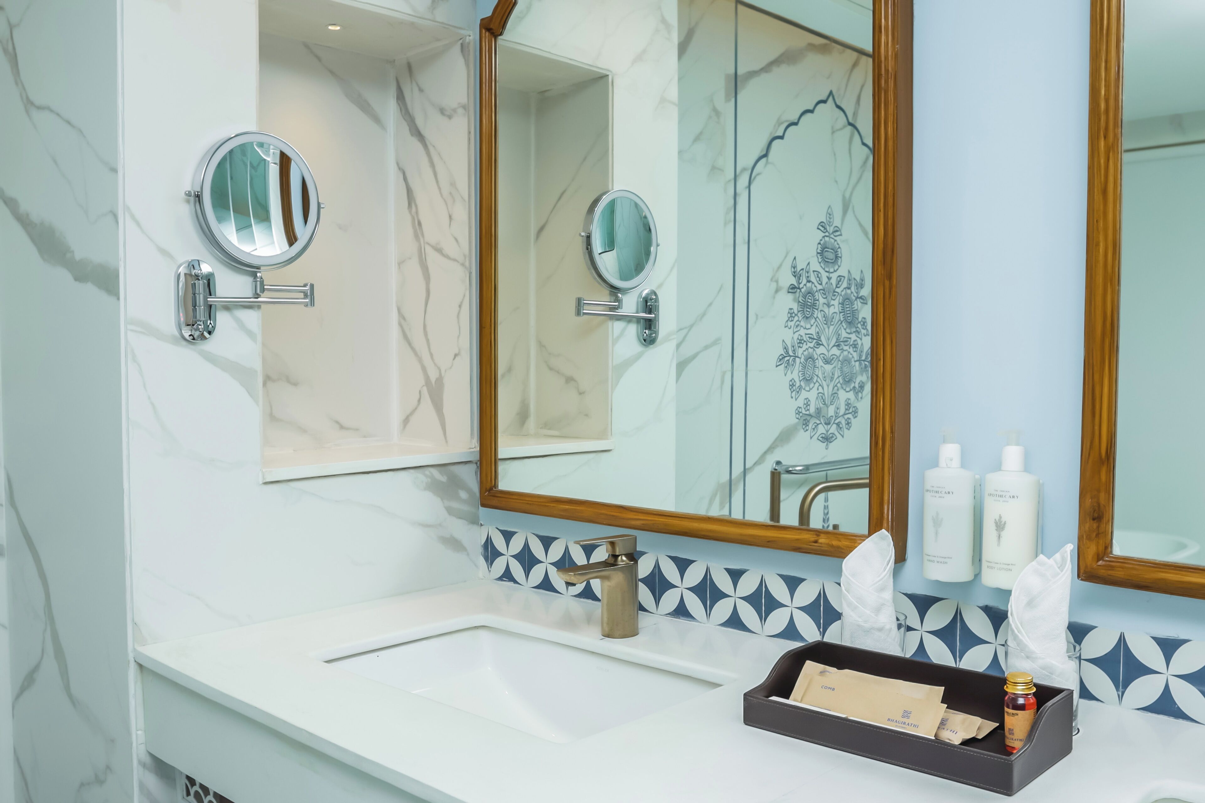 Une salle de bain avec un mur en marbre, deux miroirs ronds, un lavabo et des articles de toilette.