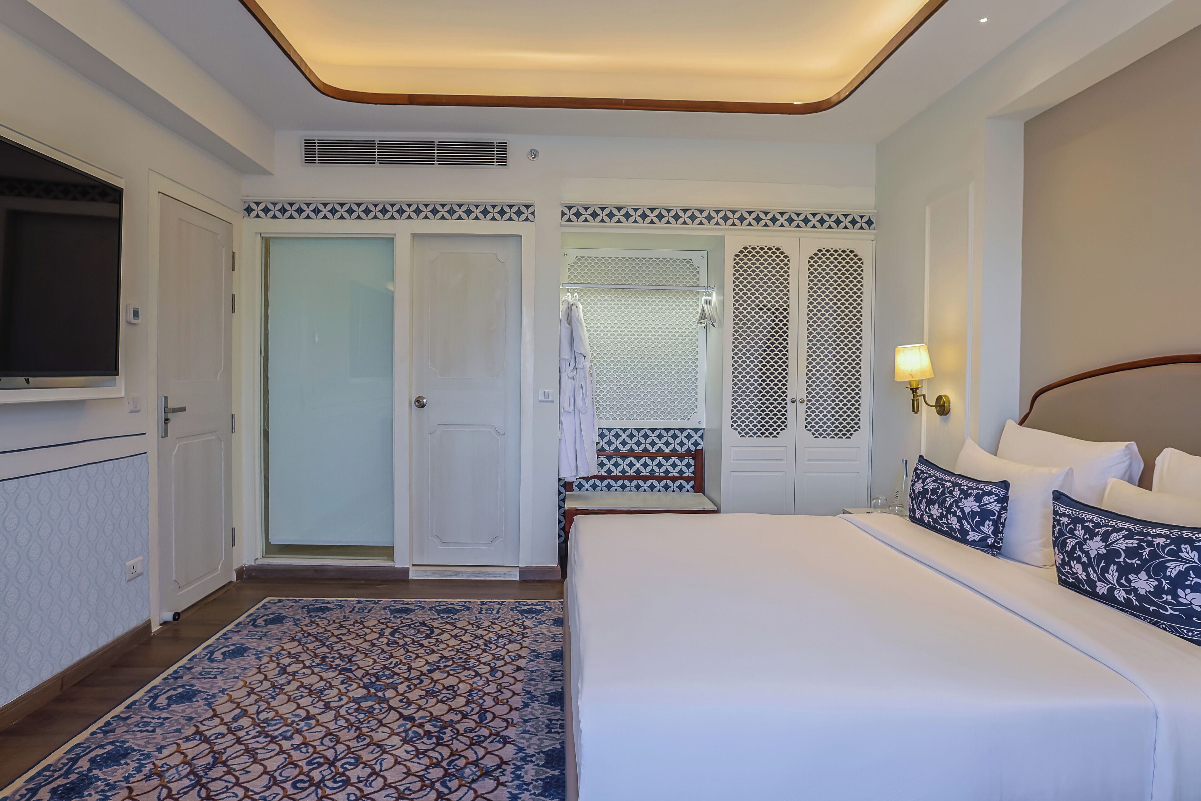 A hotel room with a bed, a TV, a patterned rug, and a door with a patterned design.