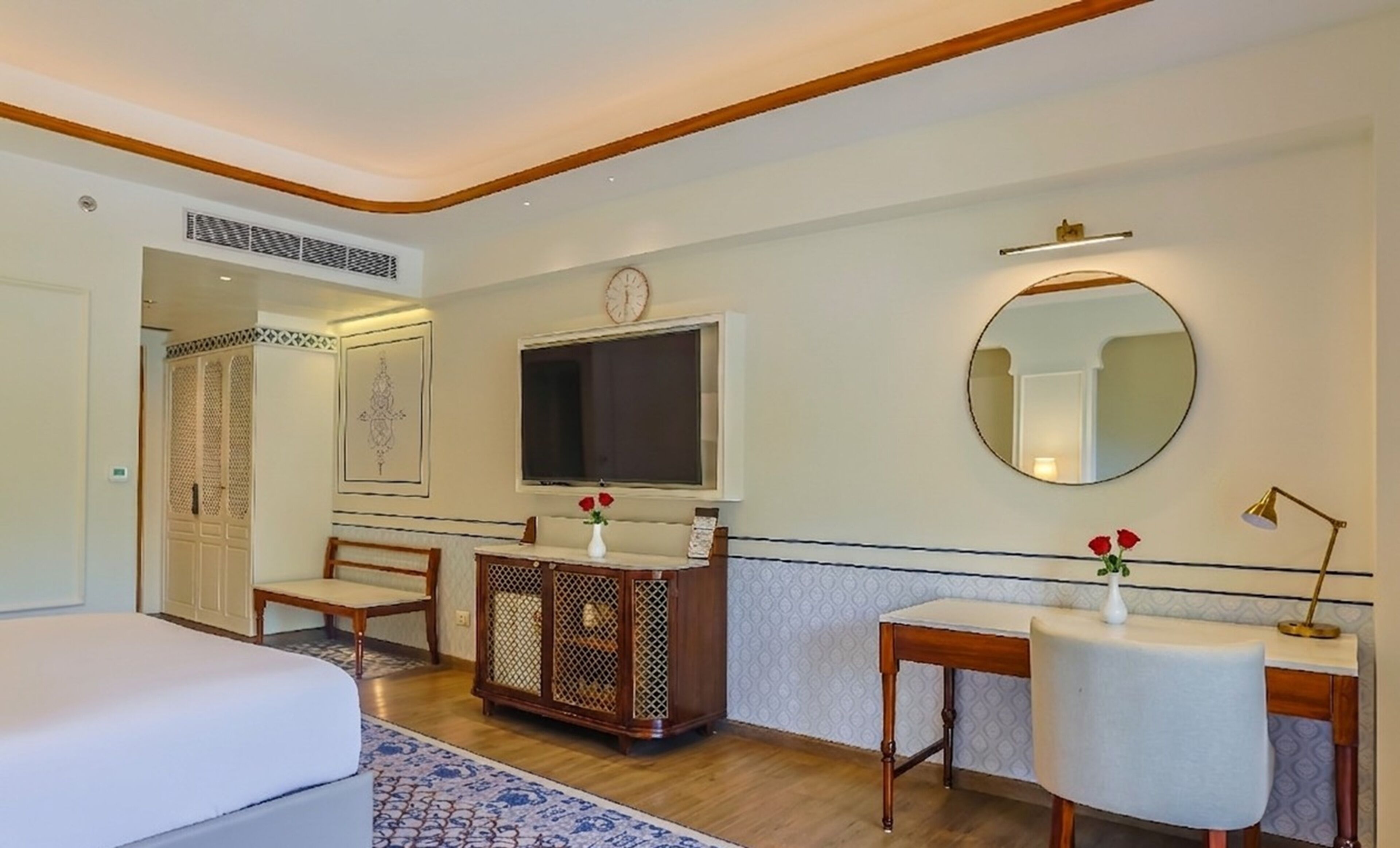 A hotel room with a bed, a desk, a chair, a TV, a mirror, and a decorative cabinet.