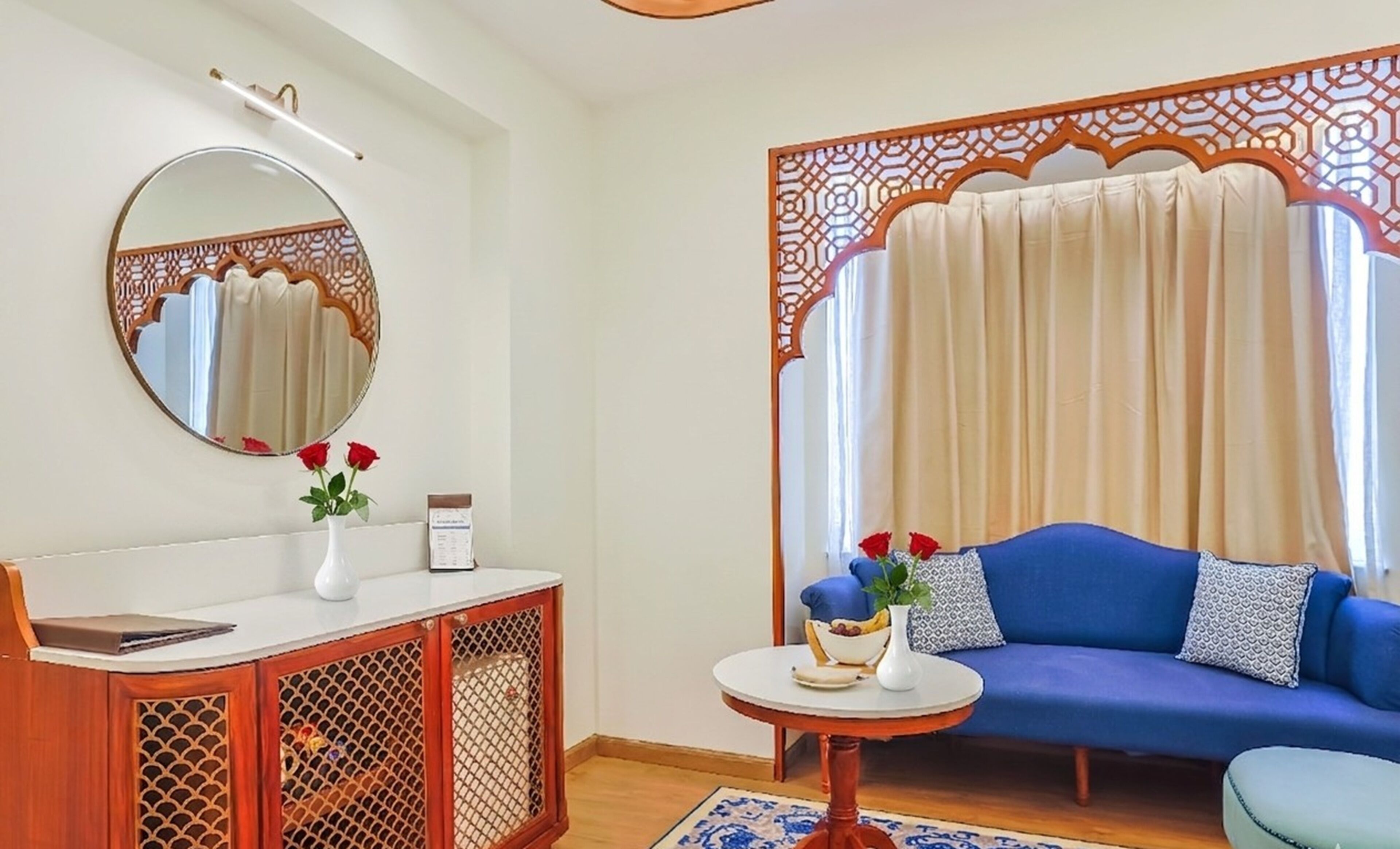 A room with a round mirror, a white console table, a blue sofa, and a decorative partition with a curtain.