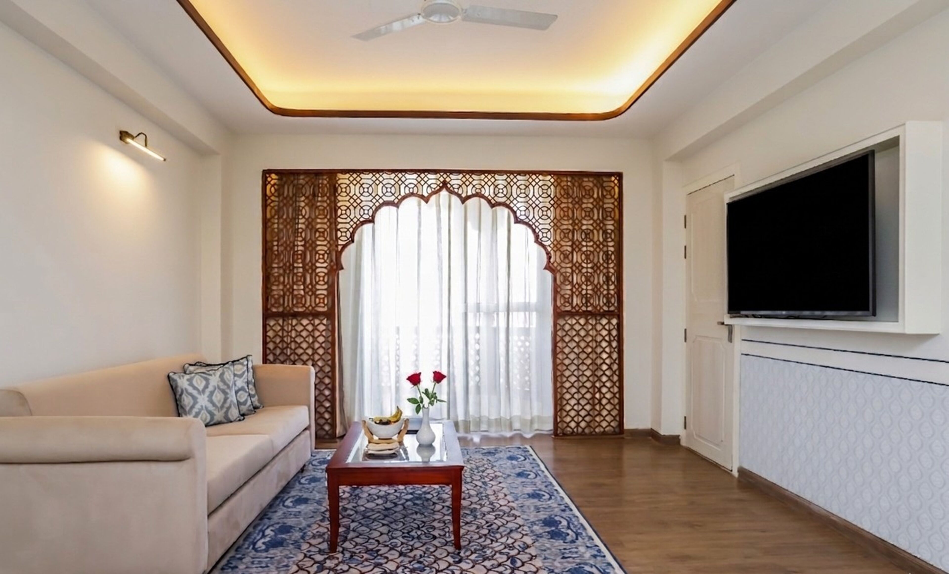 A living room with a sofa, coffee table, TV, decorative screen, and patterned rug.