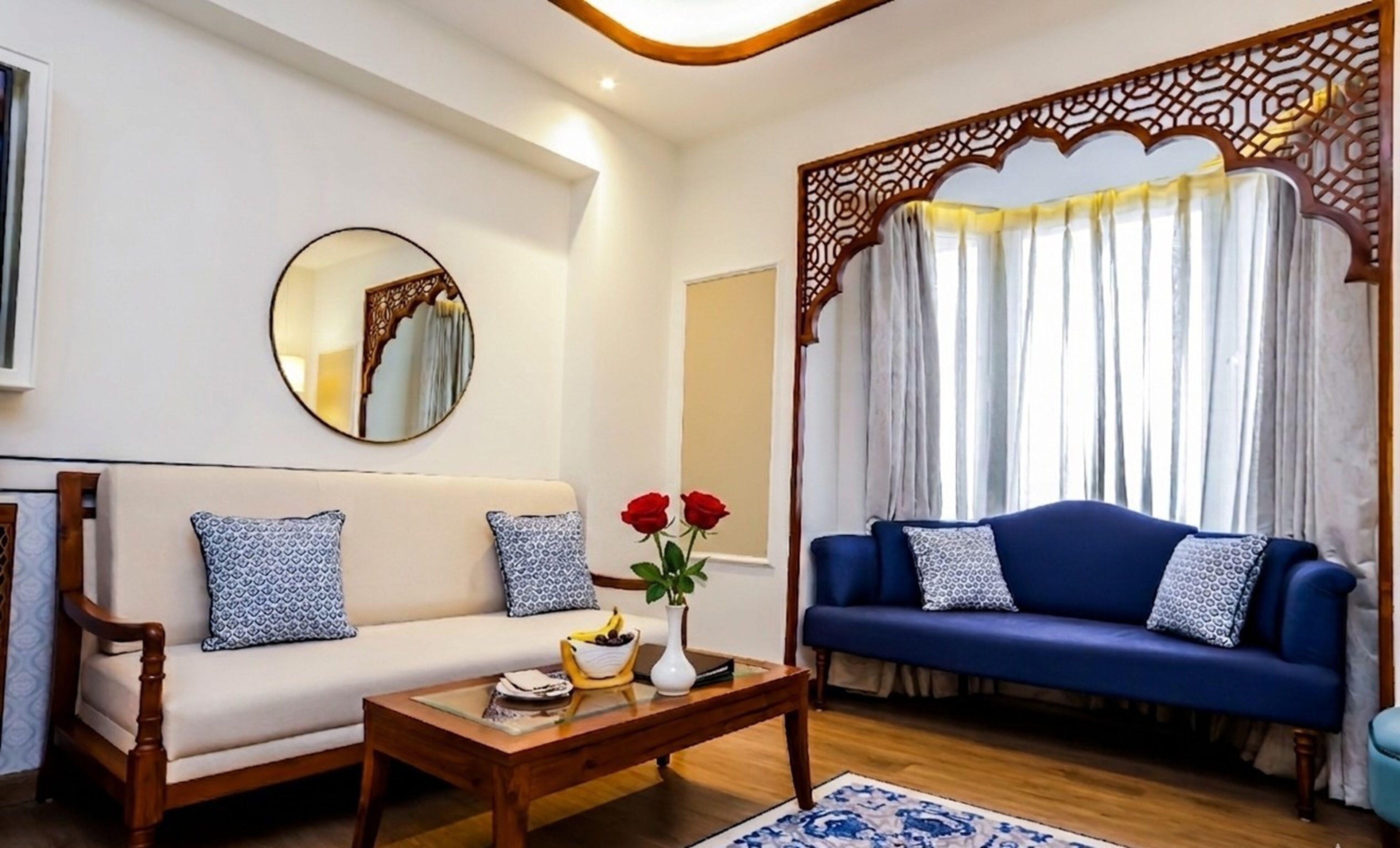 A living room with a white sofa, a blue sofa, a wooden coffee table, a mirror, and a decorative screen.