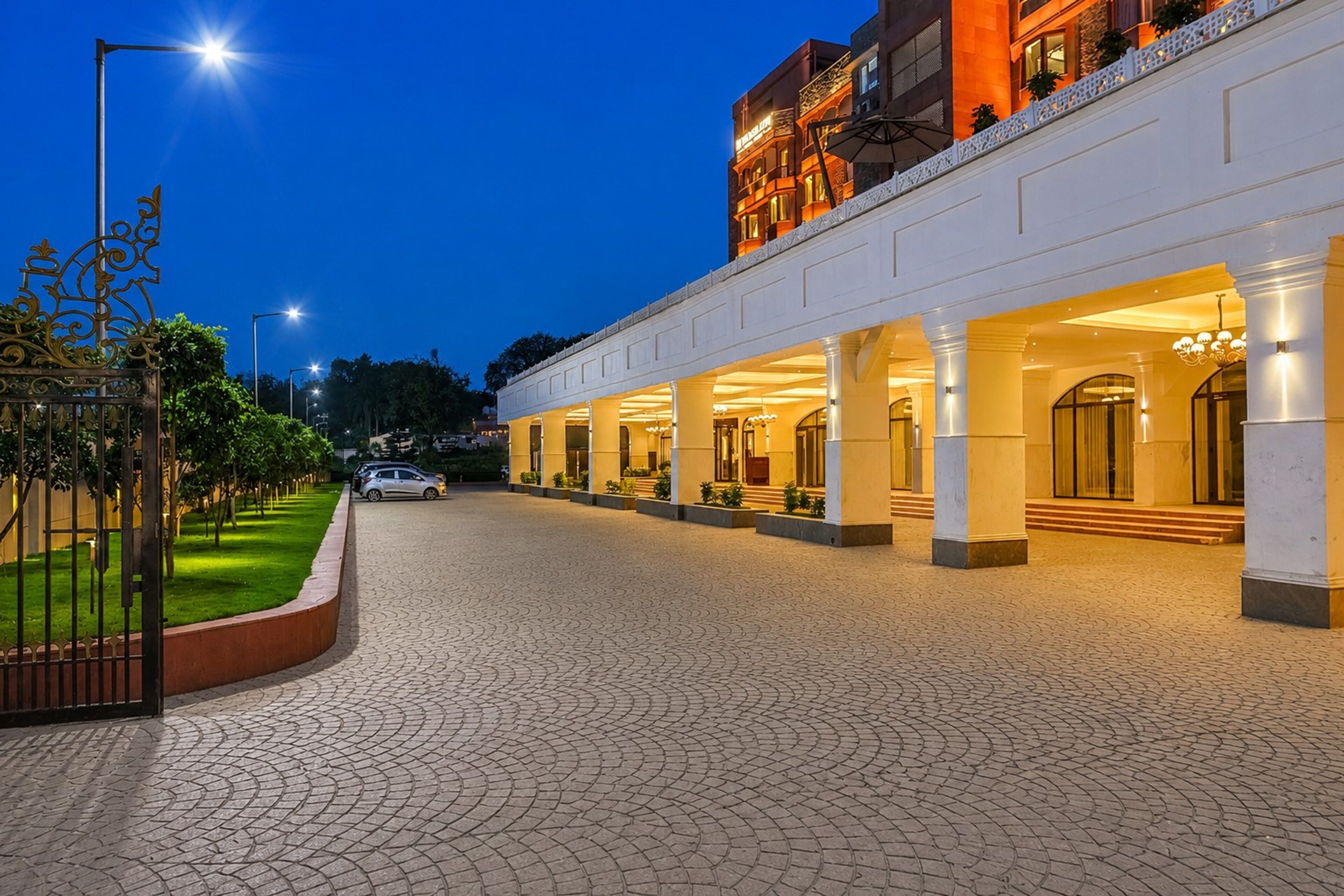 A hotel entrance with a paved driveway, a gated entrance, and a building with multiple arches and columns.