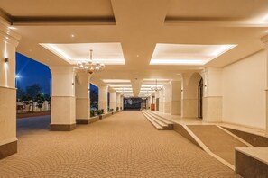 A spacious corridor with a tiled floor, white columns, and a chandelier. - Bhagirathi By Atishay (Haridwar)