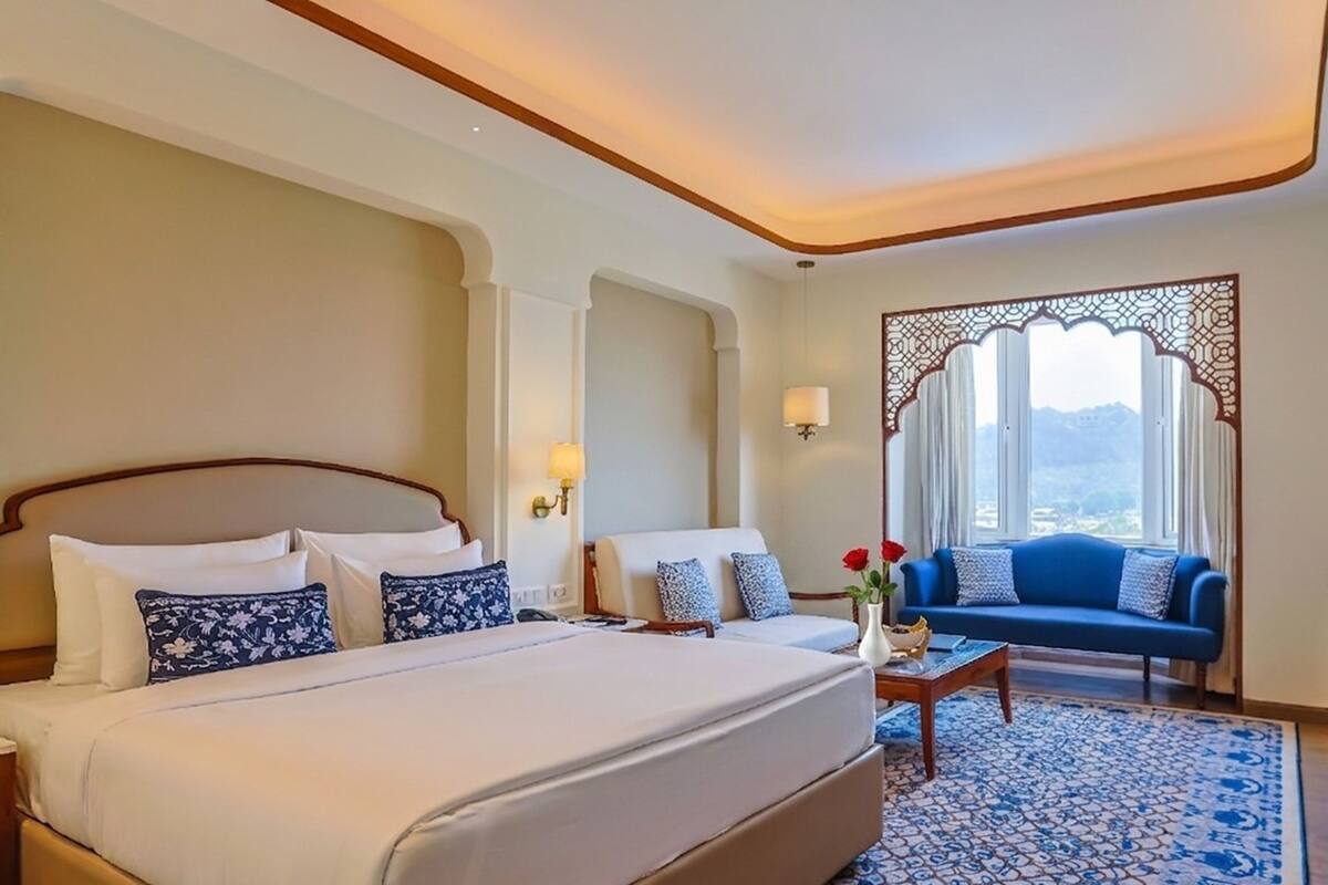A hotel room with a large bed, a sofa, a coffee table, and a view of mountains through a window with a decorative screen.