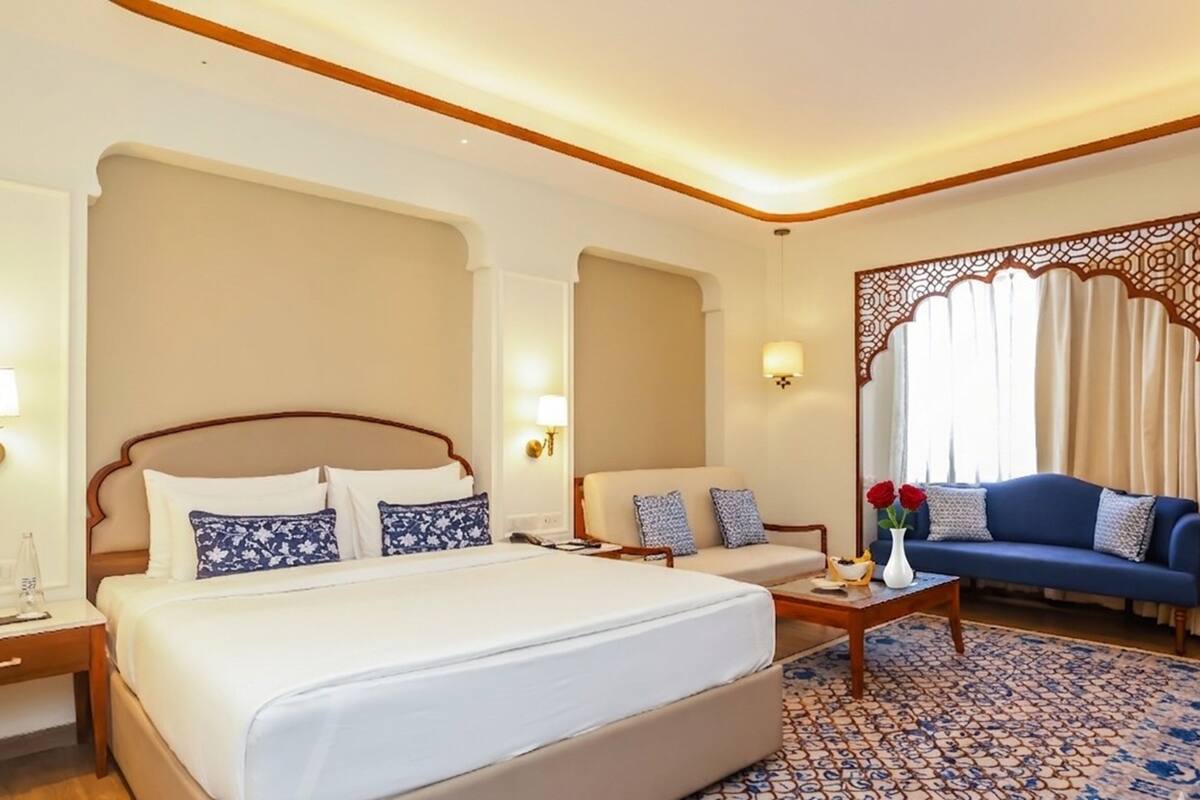 A hotel room with a large bed, a sofa, a coffee table, and a decorative screen.