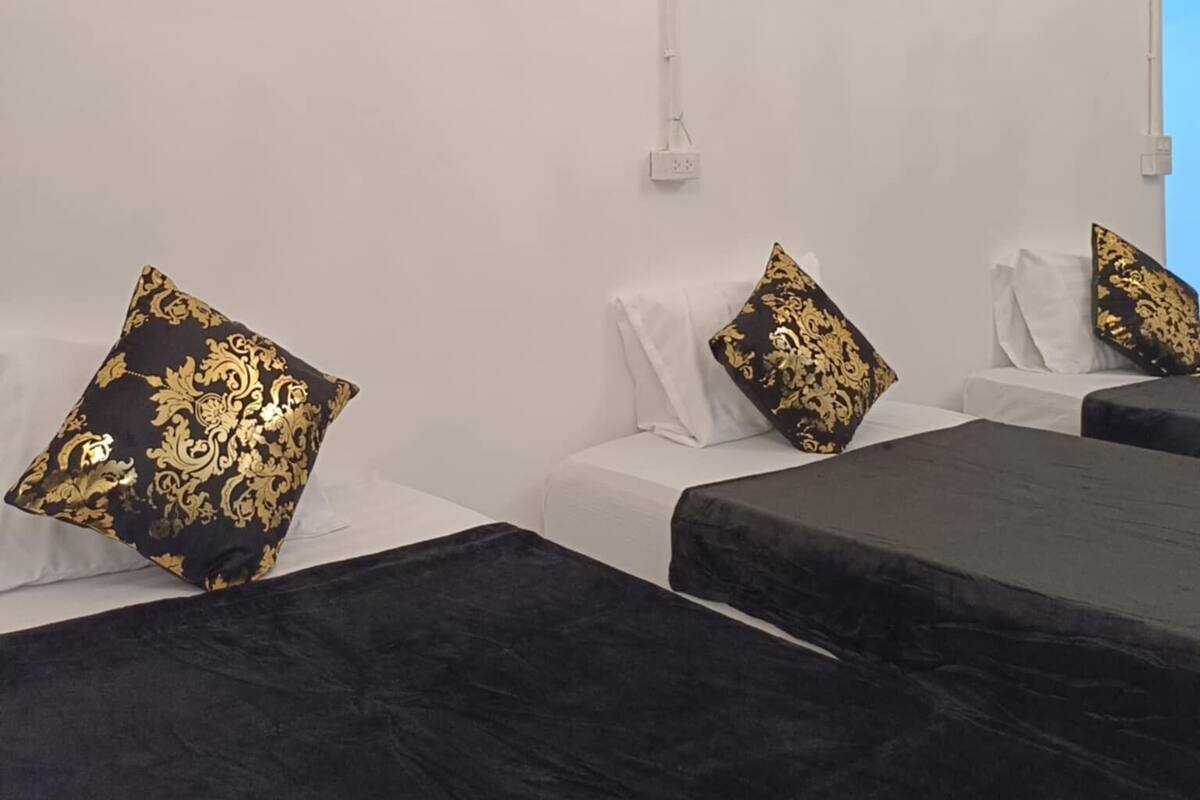 Ein Hotelzimmer mit zwei Betten, weißen Wänden und Kissen mit goldenem und schwarzem Muster.