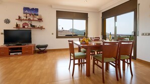 A spacious living area with a dining table, chairs, a television, and a balcony with a view. - Apartment in Blanes with Sea View Terrace (Blanes)