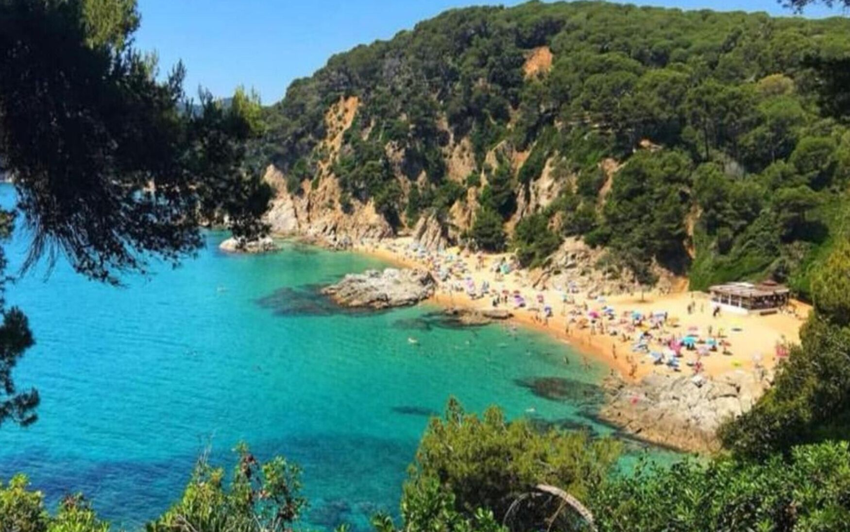 Ein Küstenstrand mit klarem türkisblauem Wasser und felsigen Klippen.