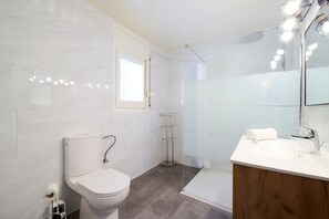 Ein modernes Badezimmer mit Toilette, einer Duschkabine aus Glas, einem Waschtisch mit Spiegel und einem Handtuch auf der Ablagefläche.