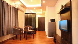 A modern living room with a wooden floor, a TV mounted on the wall, a dining table with chairs, and a sofa. - Friends Apartment Pvt.Ltd  (Nagarjun)