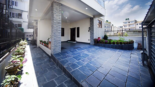 A modern building with a covered patio area, stone flooring, and potted plants. - Friends Apartment Pvt.Ltd  (Nagarjun)