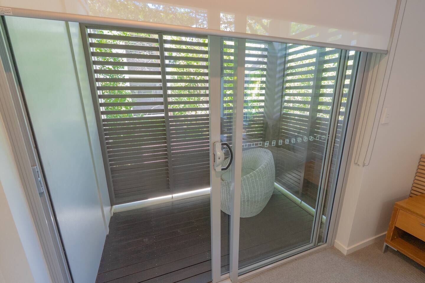 Puerta de cristal que da a un espacio exterior cubierto con una silla de mimbre adentro.
