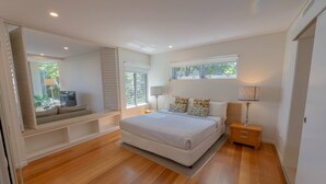 A modern bedroom with a large bed, built-in seating, and a view of greenery outside.