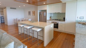A modern kitchen with a central island, bar stools, a dining area with chairs, and a built-in oven.