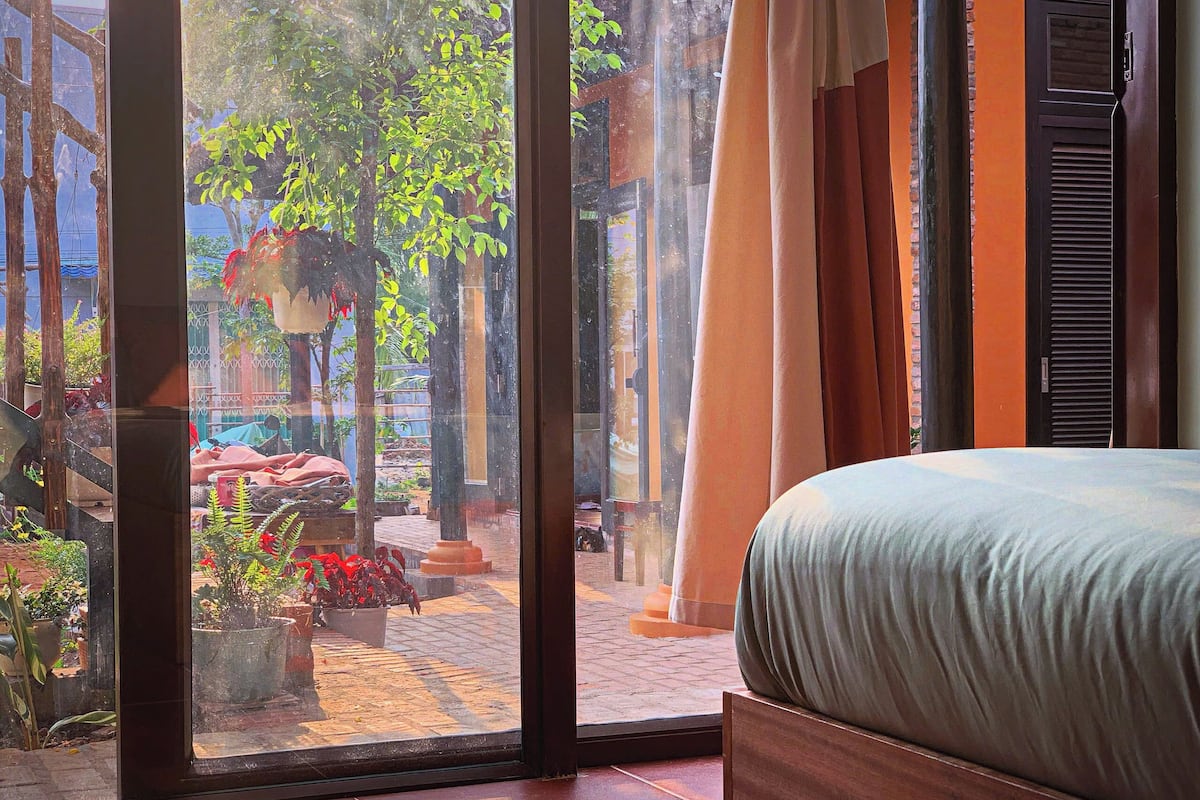 Un dormitorio con un ventanal amplio, una cama y vistas a un patio exterior con plantas y un sendero de ladrillos.