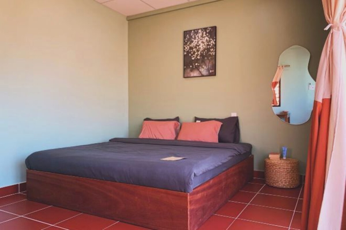 A bedroom with a bed, pillows, a wall-mounted mirror, and a small round table with a basket.