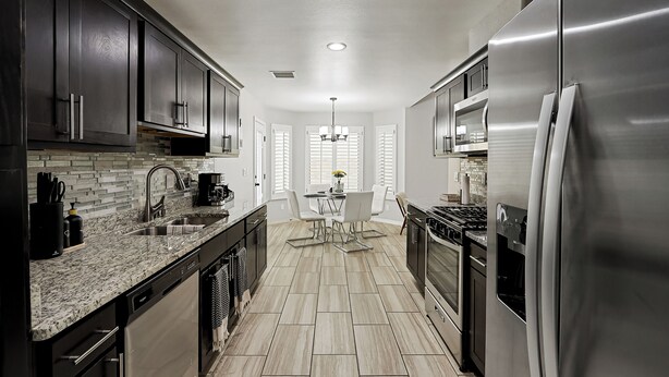 A modern kitchen with dark cabinets, stainless steel appliances, and a tiled floor.