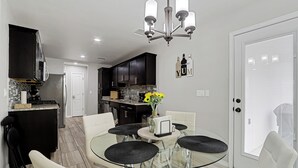 A modern kitchen with dark cabinets, a glass dining table, and a chandelier.