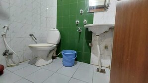 Une salle de bain avec des toilettes, un lavabo et une douche. Un seau bleu est posé sur le sol.