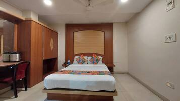 A hotel room with a bed, a desk with a chair, a wardrobe, and a ceiling fan.