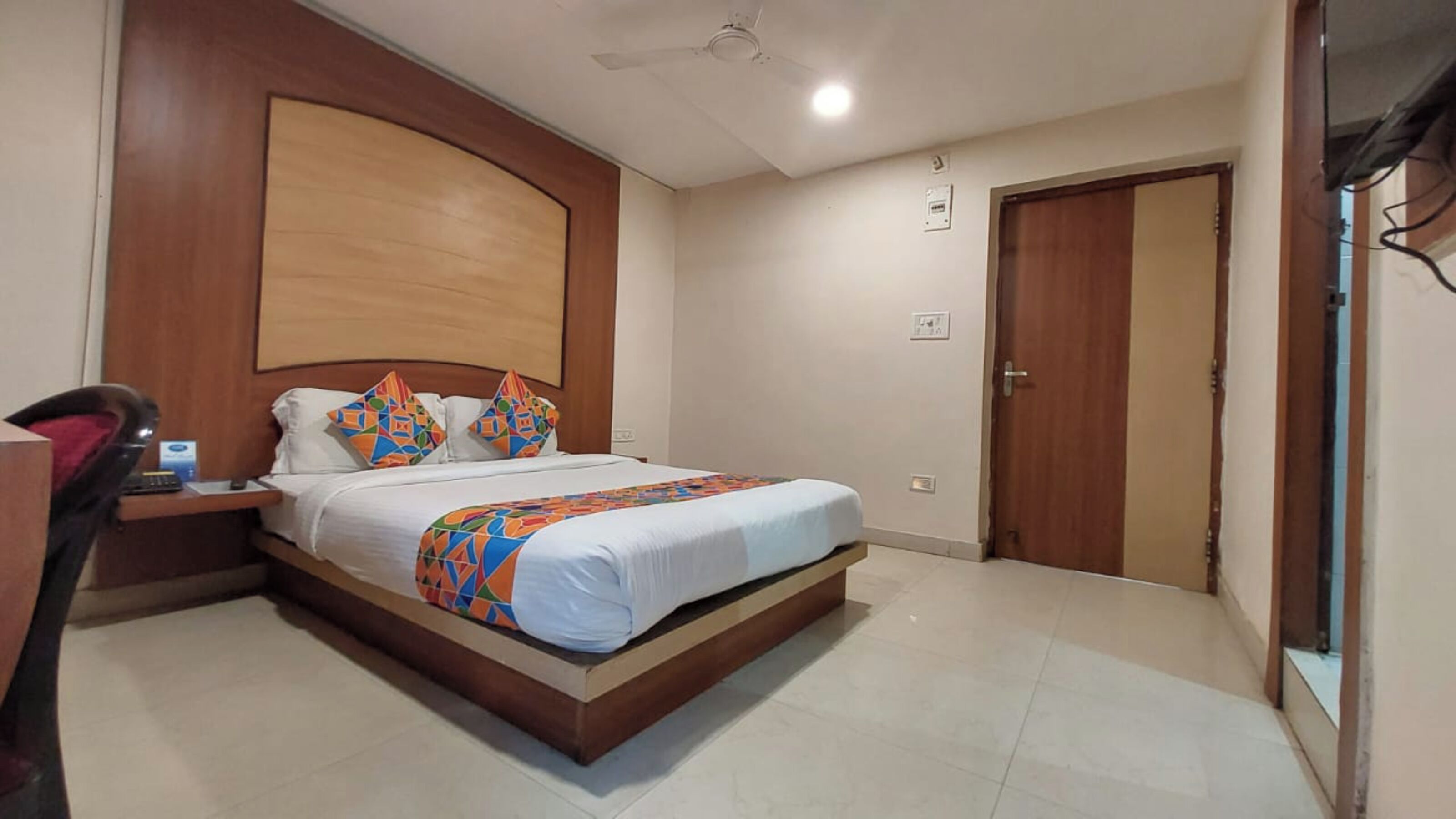 Quarto com cama, escrivaninha, cadeira, ventoinha de teto e porta.
