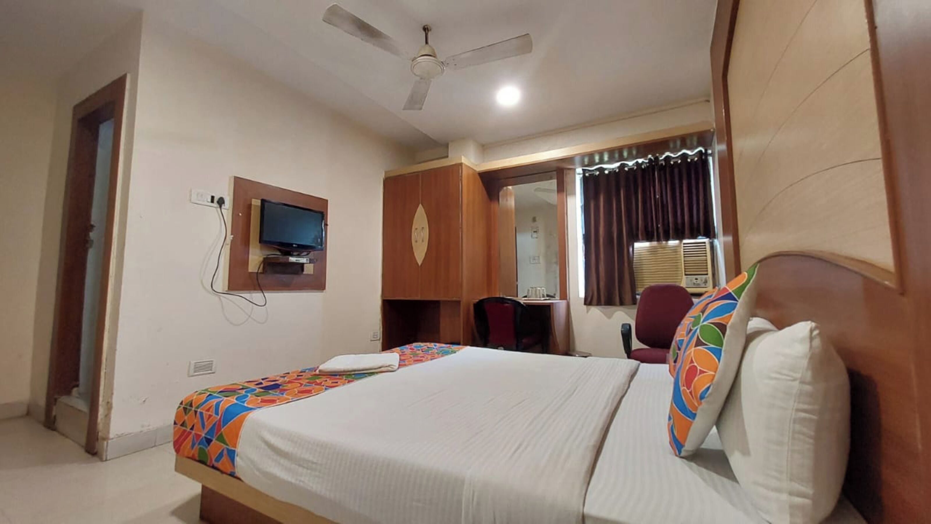 A hotel room with a bed, a desk, a chair, a television, and a ceiling fan.