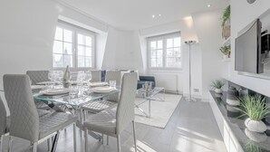 A modern dining area with a glass table, white upholstered chairs, and a blue sofa.