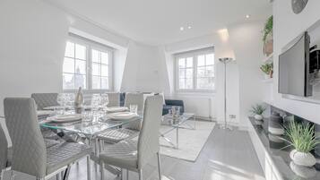 Un espace repas moderne avec une table en verre, des chaises à revêtement blanc et un canapé bleu.
