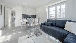 A modern living room with a dark grey sofa, a glass coffee table, and a dining area with a white table and chairs.