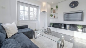 A modern living room with a grey sofa, a glass coffee table, and a large window.
