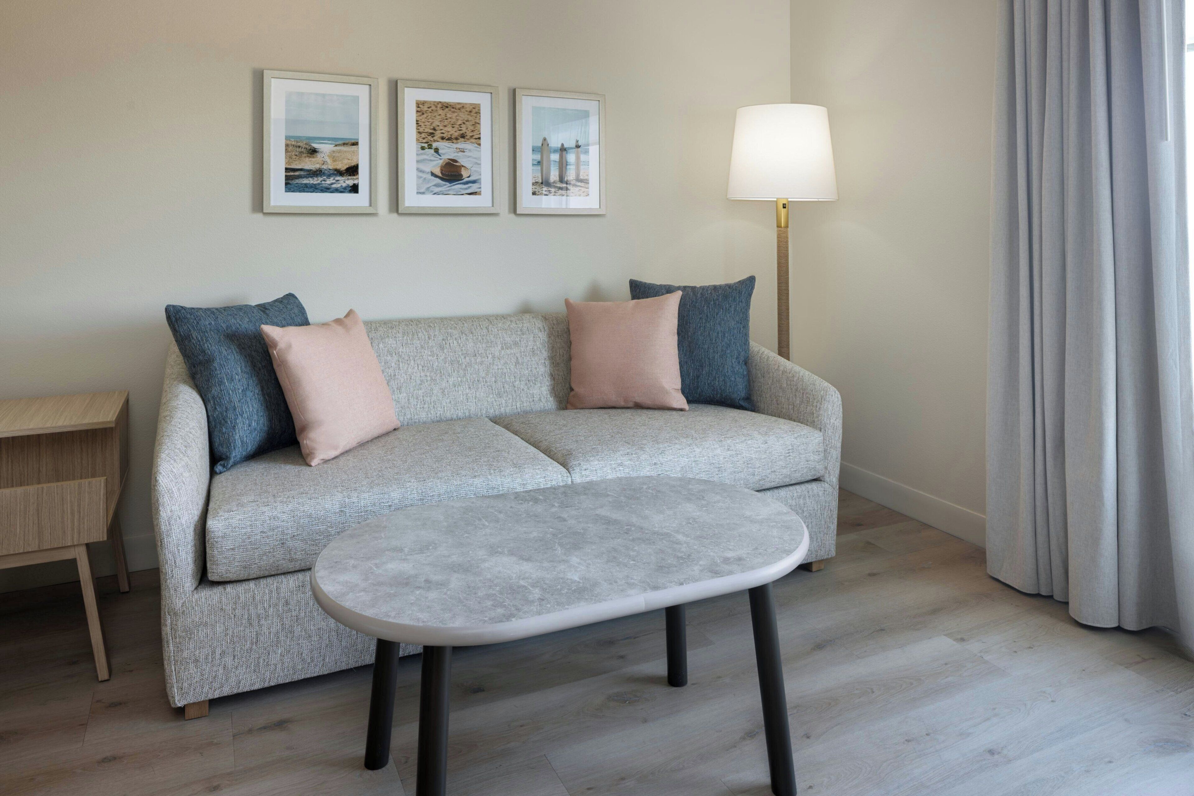 A living room with a sofa, a small round table, a lamp, and three framed pictures on the wall.