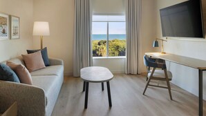 A hotel room with a sofa, a small table, a desk, a chair, a TV, and a window with a view of the sea. -  Fairfield Inn & Suites by Marriott Melbourne Beach (Indialantic)