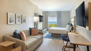 A hotel room with a bed, a sofa, a desk, a TV, and framed pictures on the wall. -  Fairfield Inn & Suites by Marriott Melbourne Beach (Indialantic)