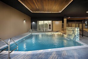 Piscina interna com borda em azulejos, escada de metal e área de estar com mesas e cadeiras.