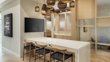 A modern kitchen with a white countertop, wooden chairs, and hanging pendant lights.