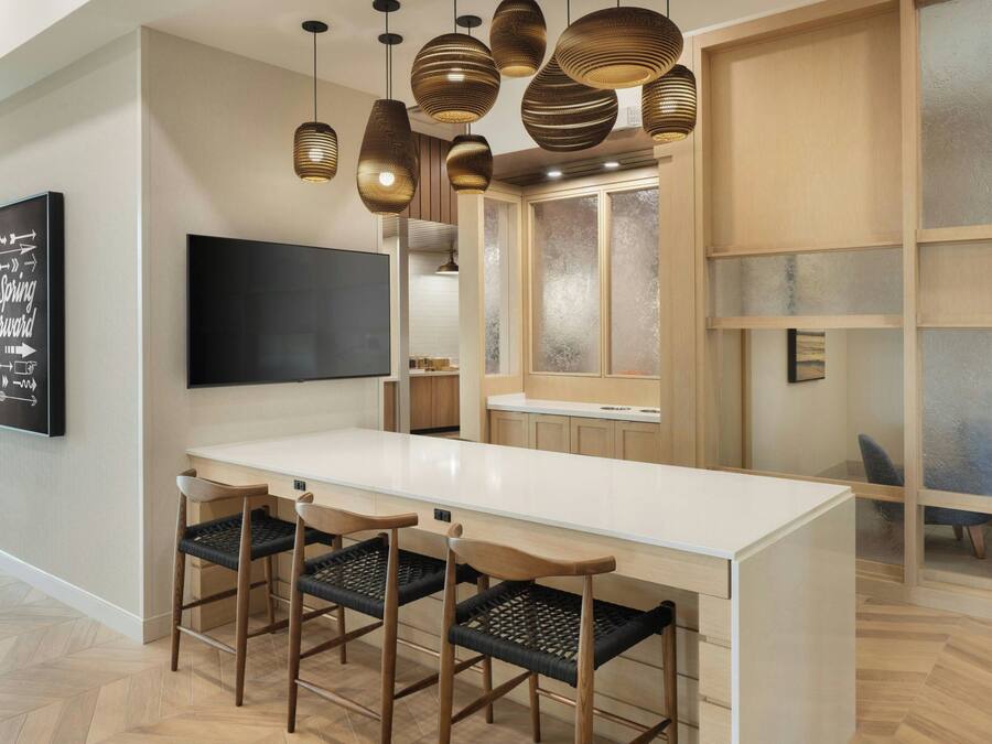 A modern kitchen with a white countertop, wooden chairs, and hanging pendant lights.