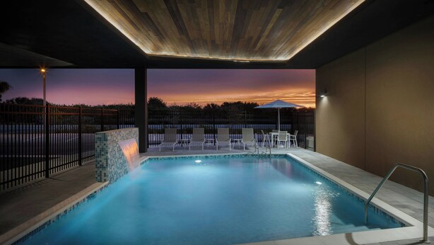 A swimming pool with a view of the sunset, surrounded by a fence, chairs, and a covered area. -  Fairfield Inn & Suites by Marriott Melbourne Beach (Indialantic)