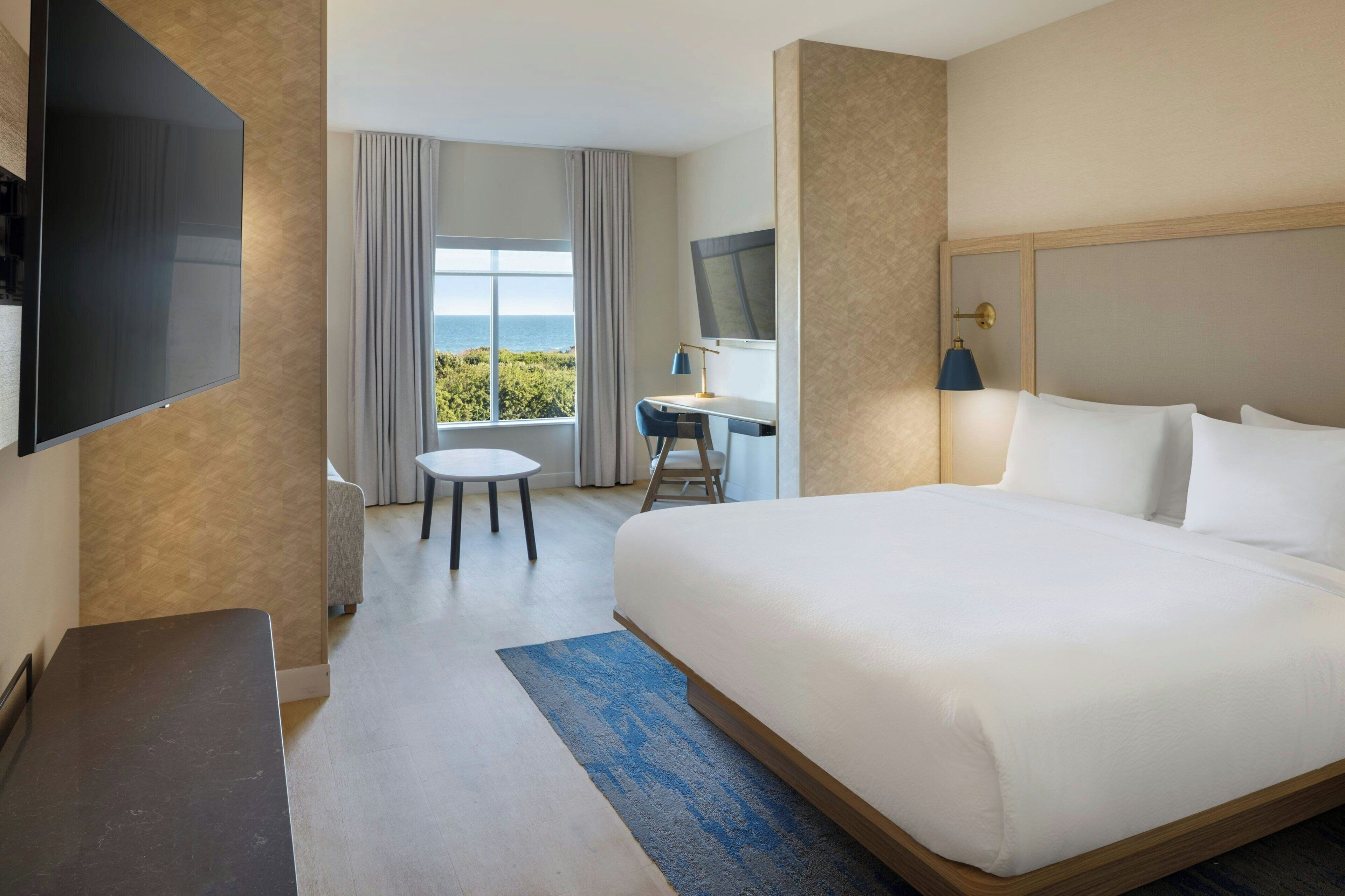 Une chambre d’hôtel avec un lit, un bureau, une télévision et une vue sur la mer.