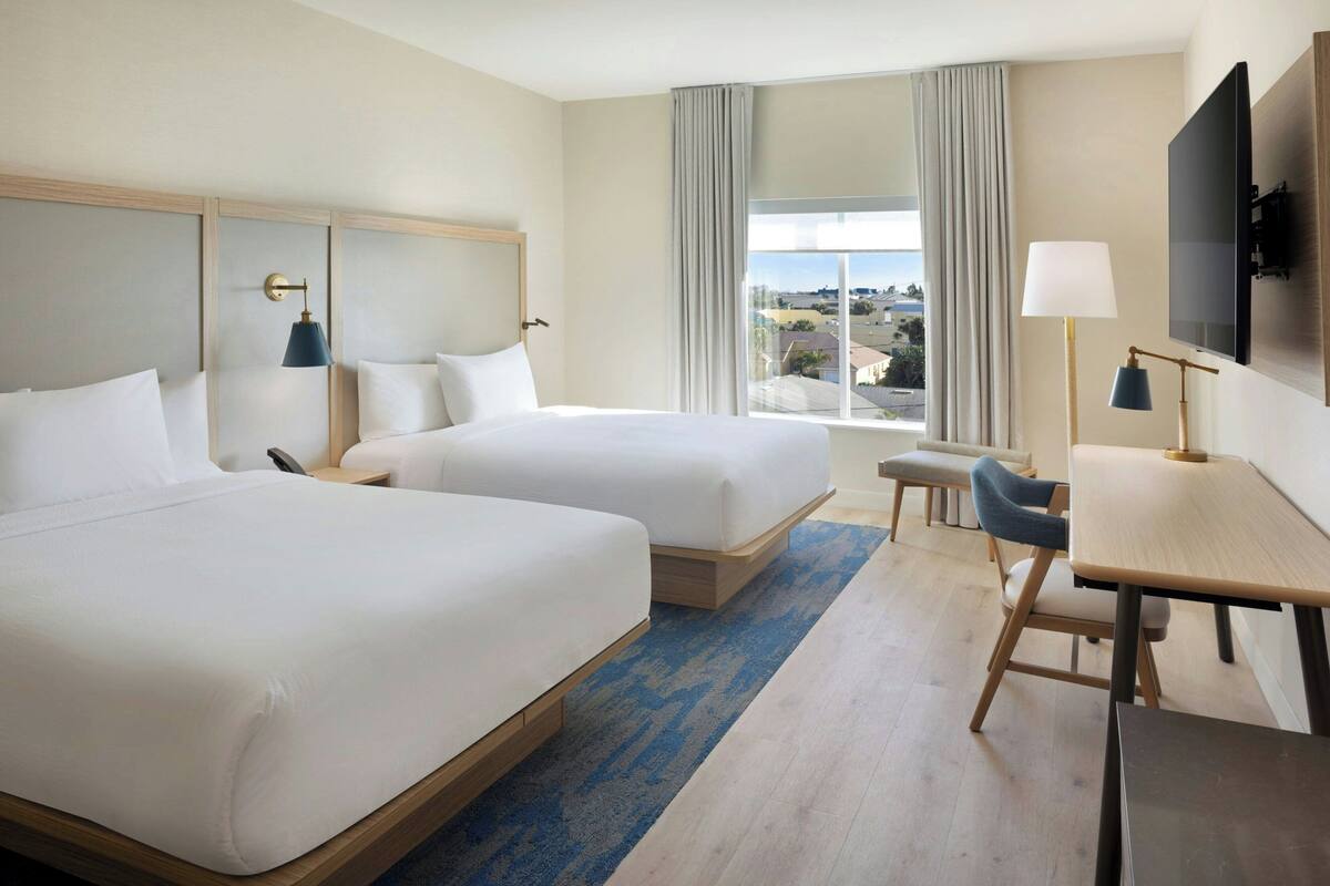 Habitación de hotel con dos camas, un escritorio, una silla, un televisor y una ventana con vistas.