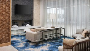 A modern living room with a flat-screen TV, a fireplace, a sofa, a coffee table, and a patterned carpet. -  Fairfield Inn & Suites by Marriott Melbourne Beach (Indialantic)