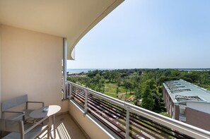 Ein Balkon mit Tisch und Stühlen, der einen Blick auf eine grüne Landschaft und Gebäude in der Ferne bietet.