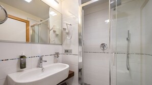 Un baño moderno con un lavamanos blanco, un box de ducha de cristal y un espejo con secadores de pelo.